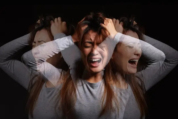 Conceptual multiple-exposure image of a woman expressing intense emotional distress and anxiety against a dark background.