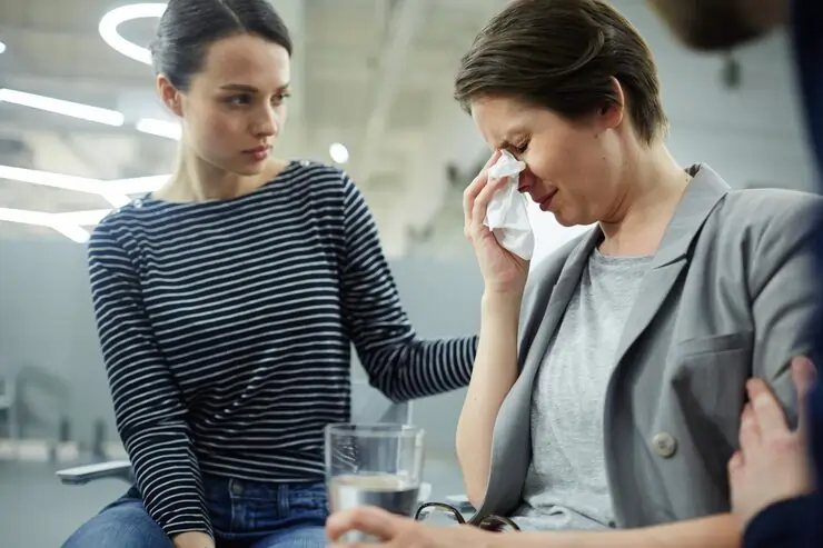 Supportive group therapy session where a woman is being comforted by others while expressing emotion in a safe environment.
